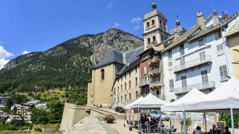 Les façades de Briançon avec une terrasse de café et les murs d’enceinte et les clochers de la collégiale