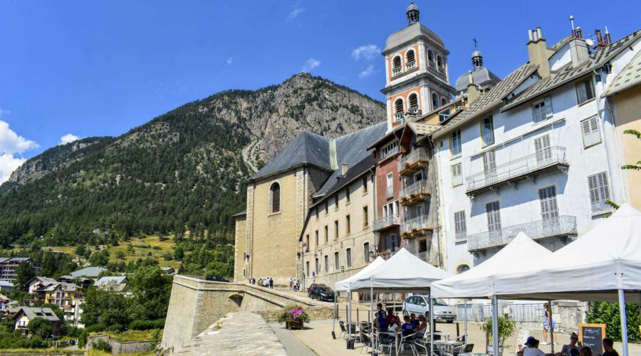 Les façades de Briançon avec une terrasse de café et les murs d’enceinte et les clochers de la collégiale