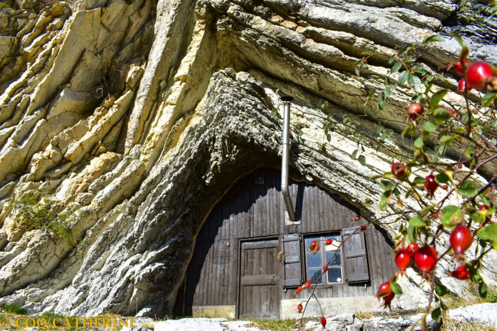 La cabane de Boules en bois qui est dans la falaise avec une cheminée et des fruits du rosier