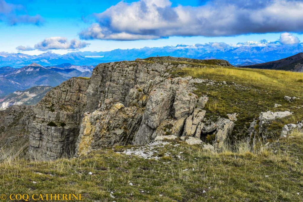 Des personnes sont sur le sommet de Coste Belle avec les falaises et en fonds les sommets des Ecrins