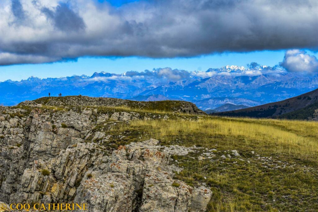 Des personnes sont sur le sommet de Coste Belle avec les falaises et en fonds les sommets des Ecrins