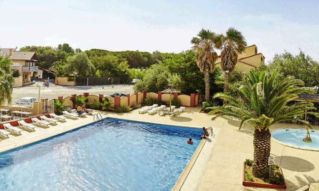 Les piscines du Camping La Presqu’île de Barcarès avec des palmiers et des chaises longues