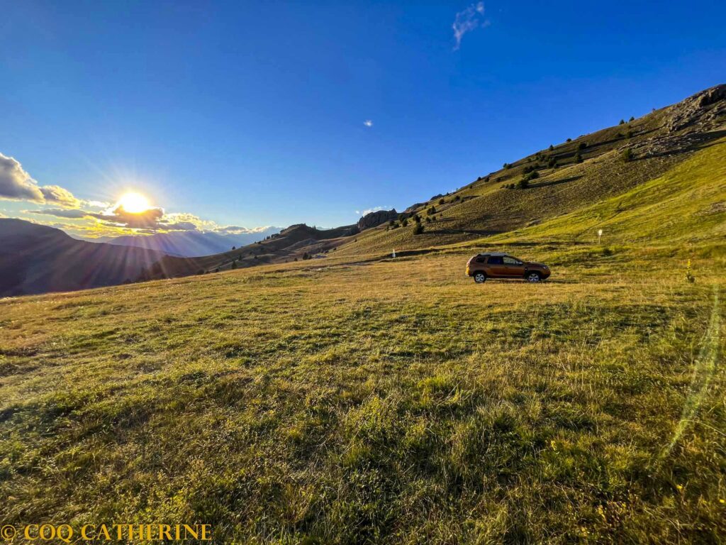 le champs d’herbe du parking des Couniets avec une voiture dans la montagne