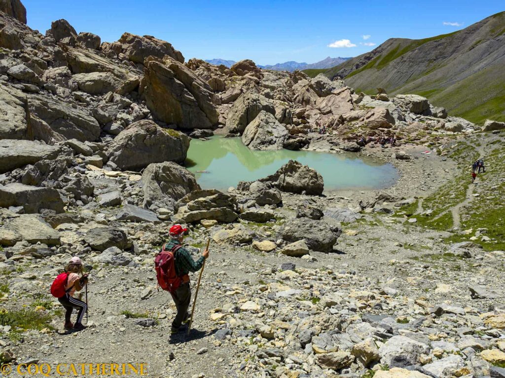 Le lac des neufs couleurs de la Mortice en randonnée entre les blocs de rocher et 2 randonneurs