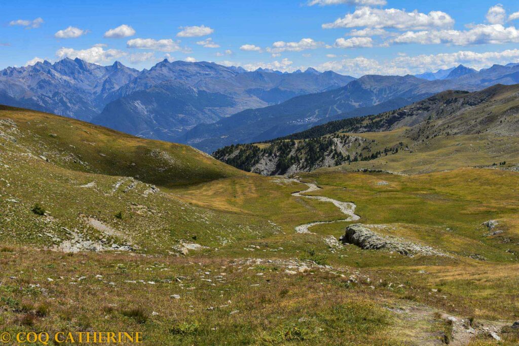 Vue sur les alpages de la cabane de l’Alp avec un torrent qui serpente et le panorama sur les montagnes