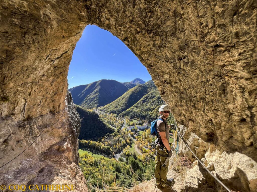 Un homme est à la sortie d’une grotte avec le câble de la via ferrata et le panorama sur les montagne et Digne les Bains via ferrata digne les bains coq (30 of 70)