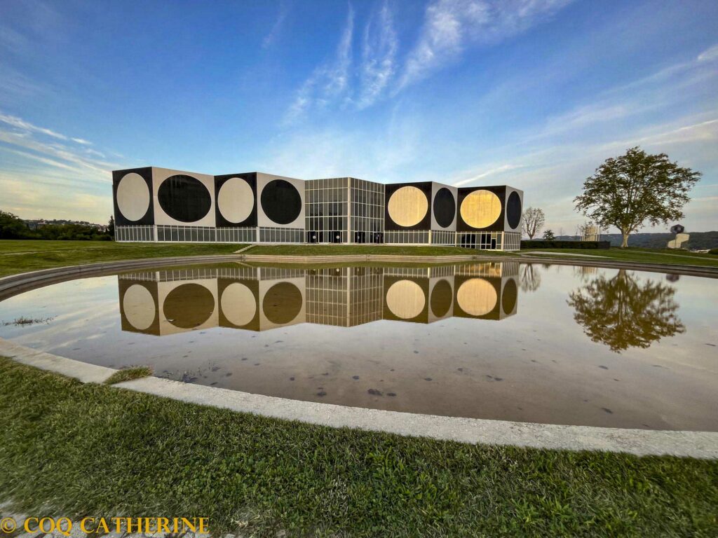 La fondation Vasarely d’Aix en Provence avec le reflet du bâtiment sur l’eau. Il est composé de carrés et de ronds, et un arbre est sur le côté