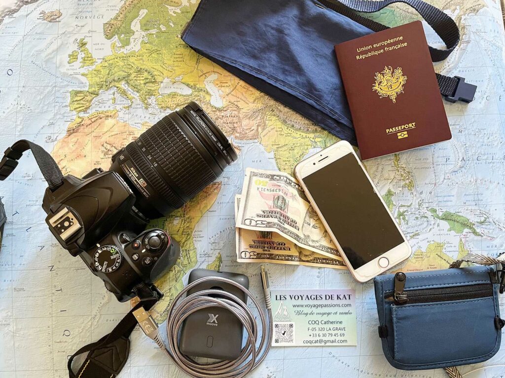 Photo d’une carte du monde avec un appareil photo, un téléphone, des dollars, une pochette, un câble et un power Bank preparer son voyage 01 coq