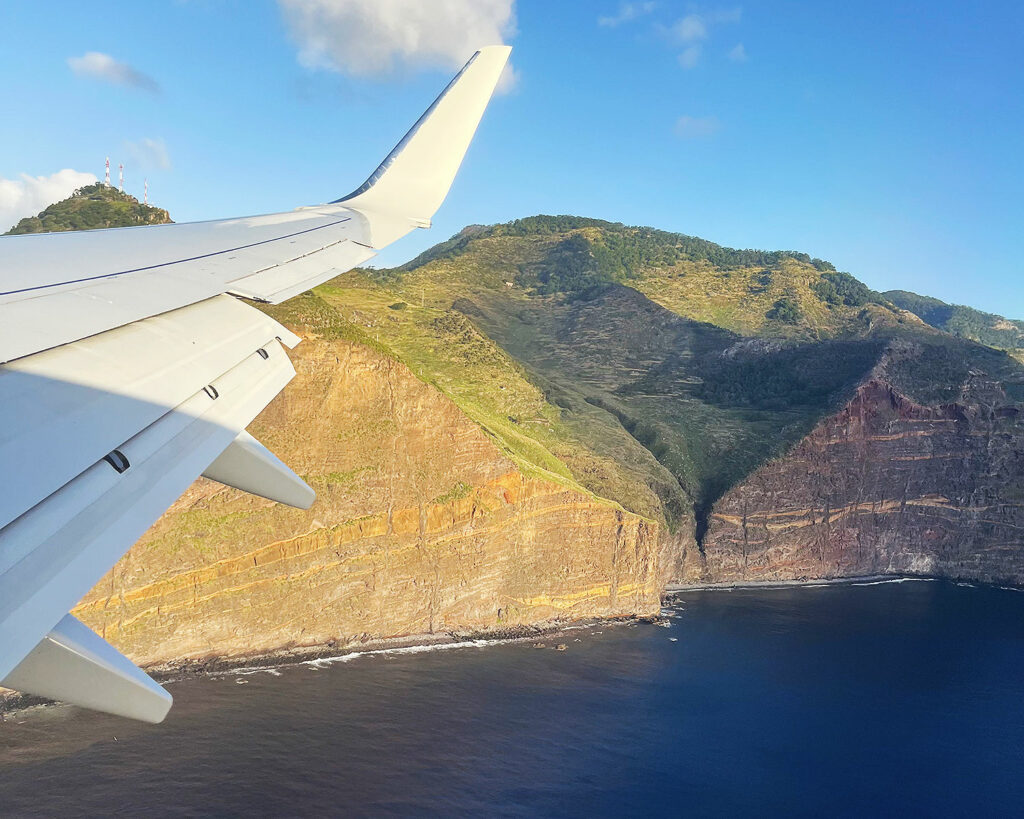 une aile d’avion avec les falaises de l’ile de Madère en arrière-plan avec la mer
