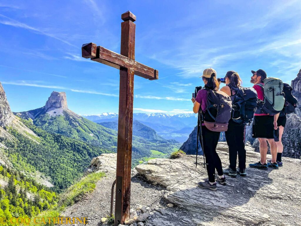 Un groupe de randonneurs avec une croix au Pas de l’Aiguille dans le Vercors avec le panorama sur le Mont Aiguille