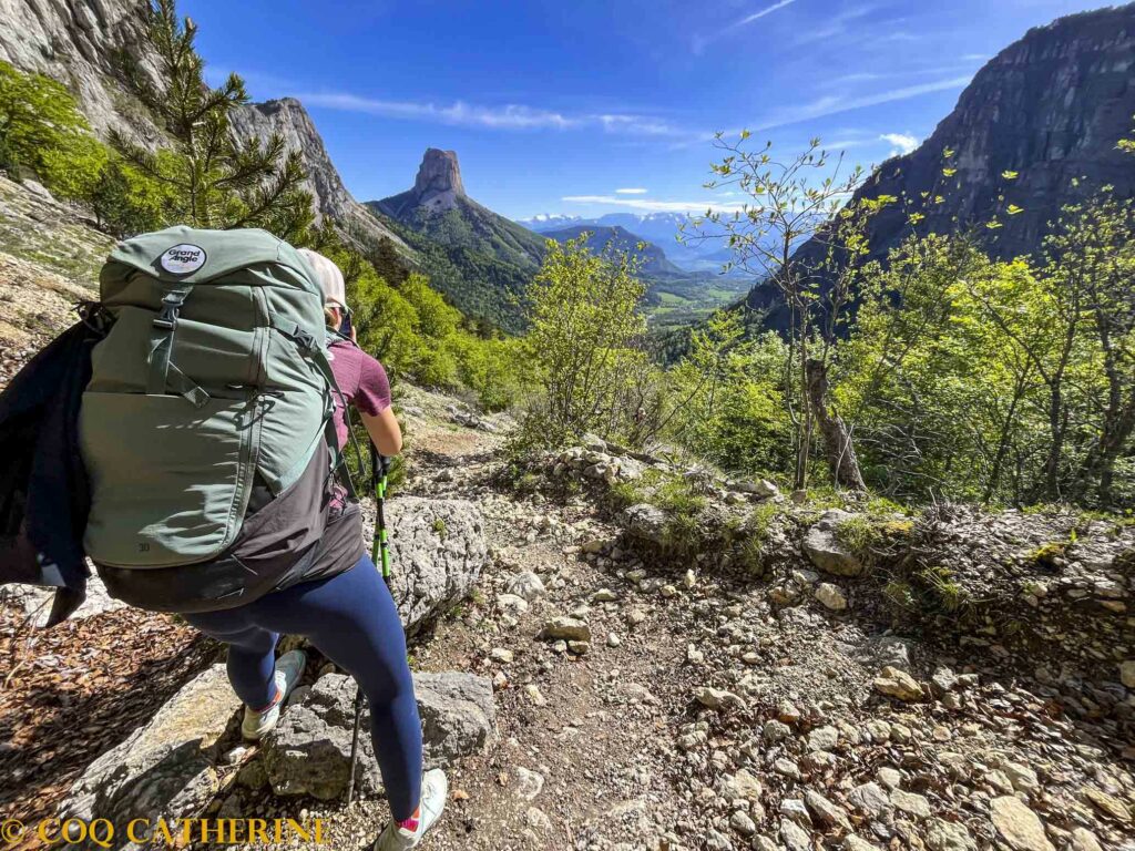 Un randonneur de dos avec son sac à dos face à la montagne et le Mont aiguille