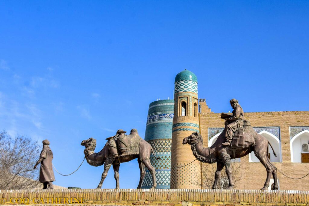 Vue sur le minaret Kalta Minor de Khiva avec les statues d’une caravane de chameaux